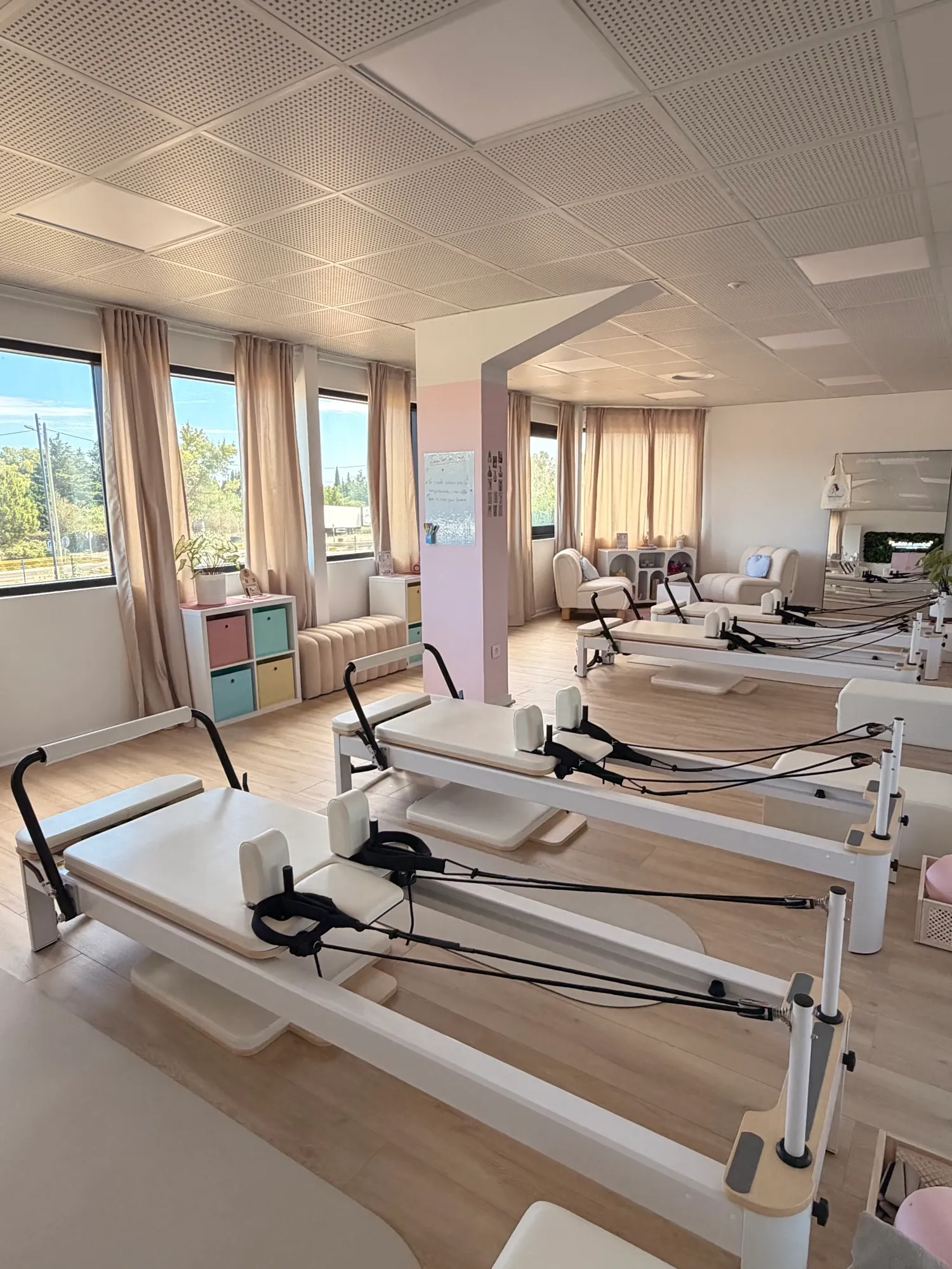 La salle du studio : Reformers alignés devant les grandes fenêtres, casiers pastel et coin salon