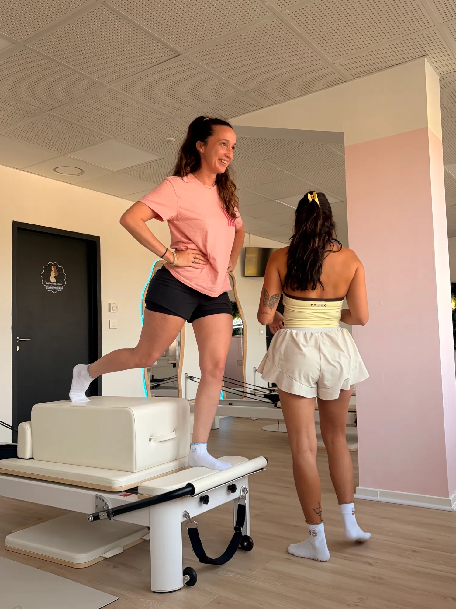 La coach debout sur un Reformer pendant un cours, une élève à ses côtés